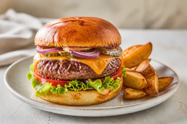 Burger maison au steak de bœuf, cheddar fondu, tomate, salade, cornichons et pain doré