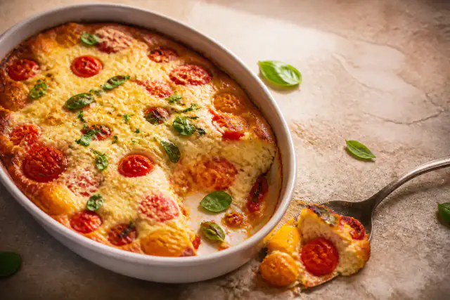 Clafoutis salé doré aux tomates cerises, Parmesan et basilic dans un plat en céramique