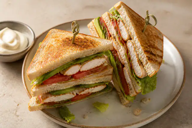 Club sandwich triangulaire à trois étages avec poulet, avocat, mayonnaise, tomate et salade