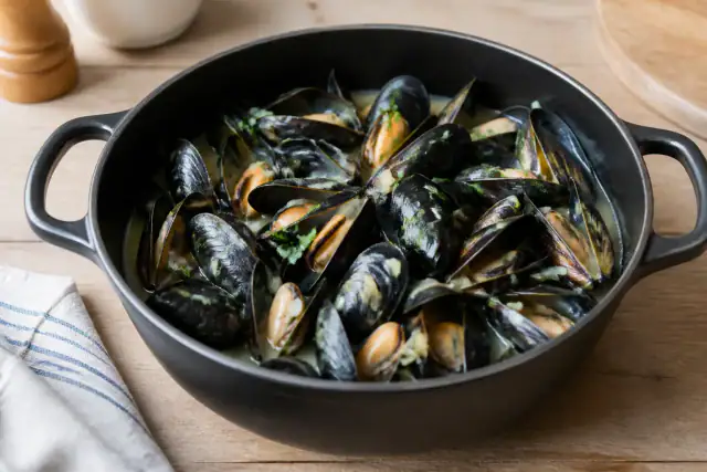 Moules marinières ouvertes dans une cocotte avec échalotes, persil et vin blanc