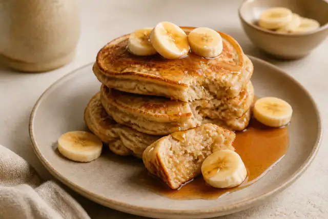 Pile de pancakes à la banane avec rondelles de fruit et sirop d’érable coulant