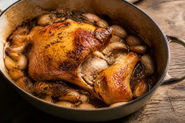 Poulet rôti en cocotte entouré de gousses d’ail confites et de thym