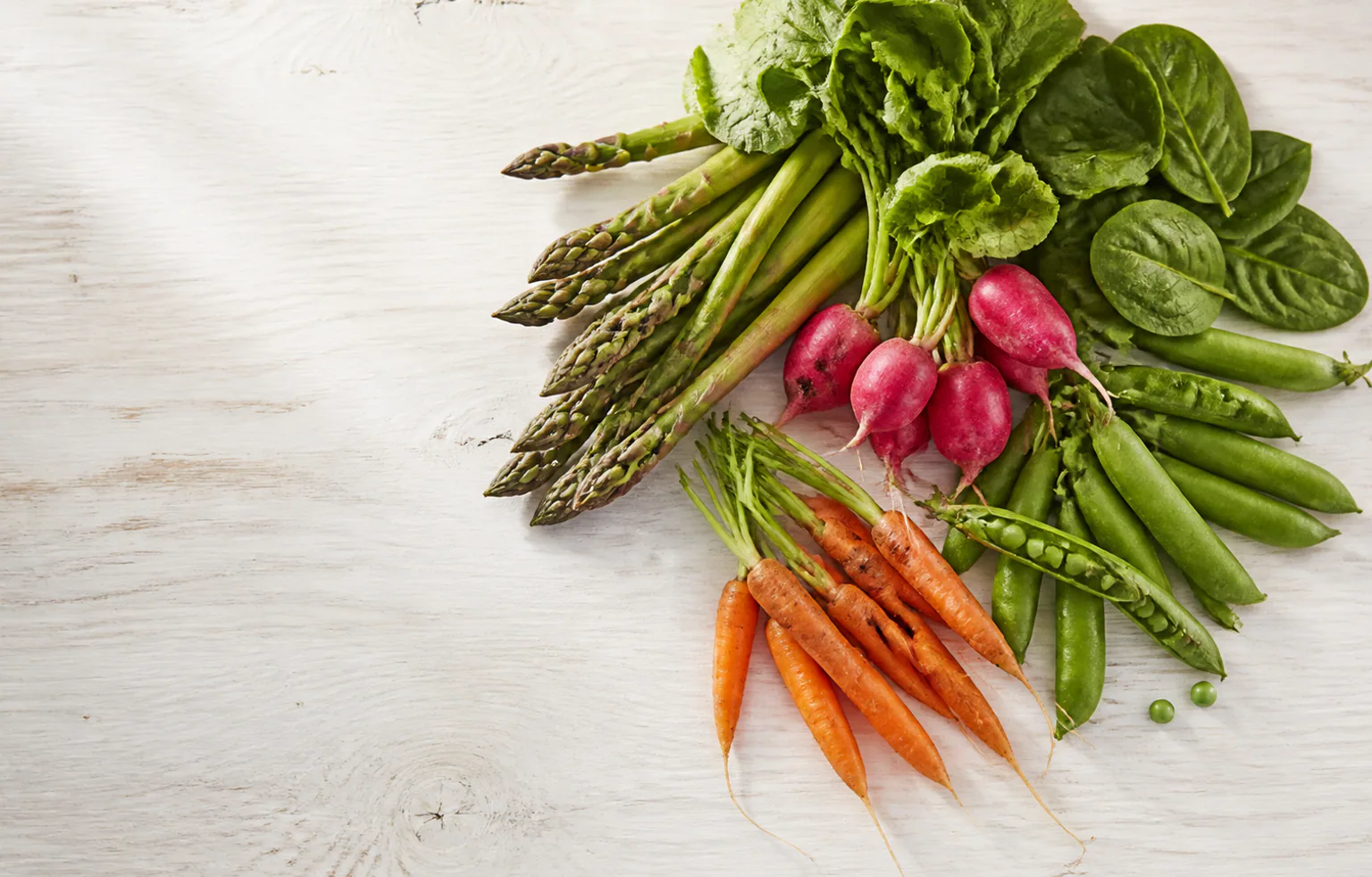 Asperges vertes, radis et petits pois frais posés sur un plan de travail de cuisine au printemps